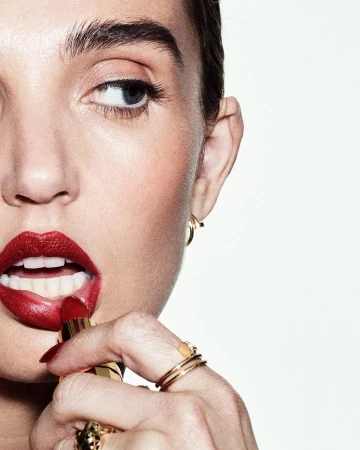 Close-up of a woman applying bright red lipstick with a gold tube against a clean white background