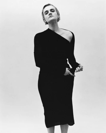 Model with short hair wearing a long black asymmetric dress against a plain light background