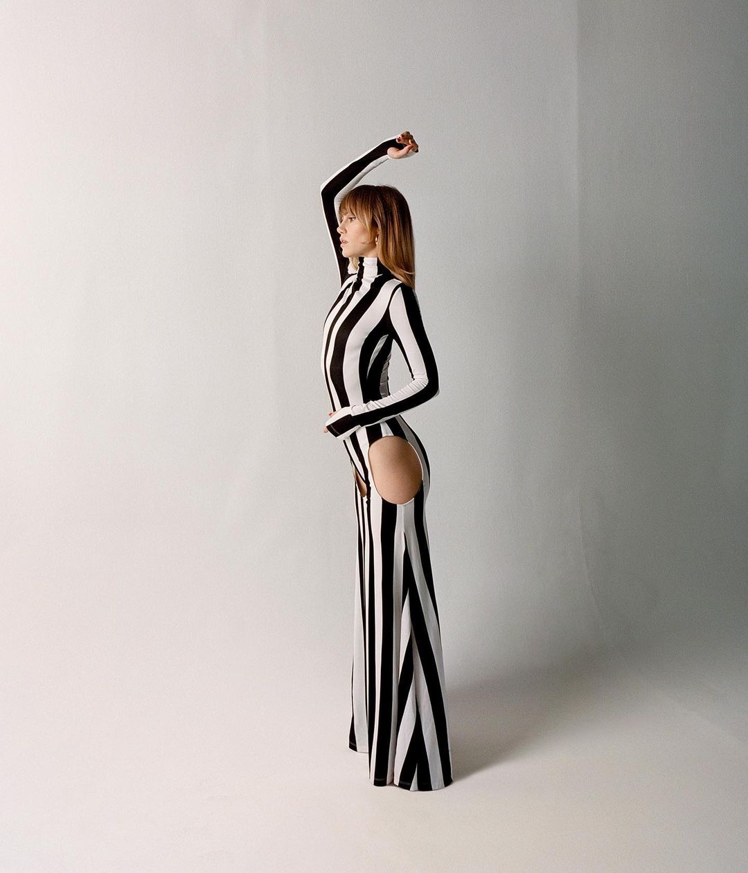Model in a black and white striped dress with side cutout posing against a white seamless background