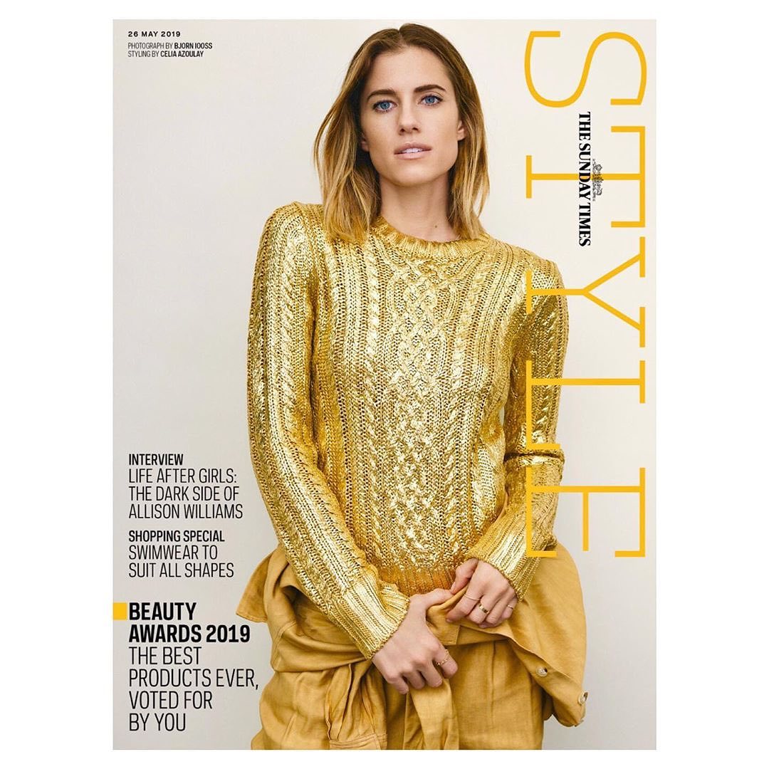 Magazine cover featuring adult female fashion model with blonde hair wearing a shiny gold sweater and tan bottoms in an indoor setting.