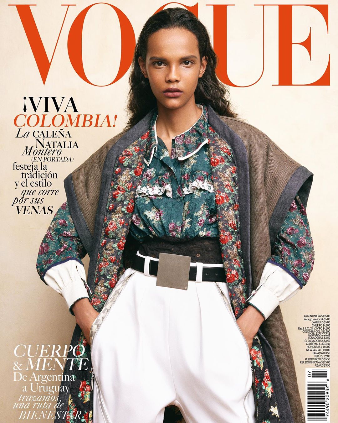 Vogue magazine cover featuring a model in a floral blouse, white pants, and a brown coat, set against a soft beige background.