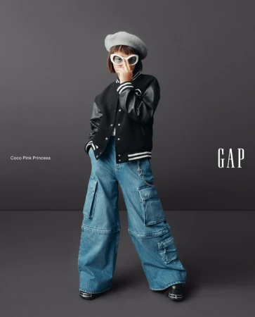 Young girl in stylish streetwear fashion poses in a studio wearing a beret, letterman jacket, and baggy jeans for a Gap ad.