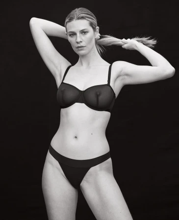 Monochrome portrait of a woman in black underwear adjusting her hair against a dark background