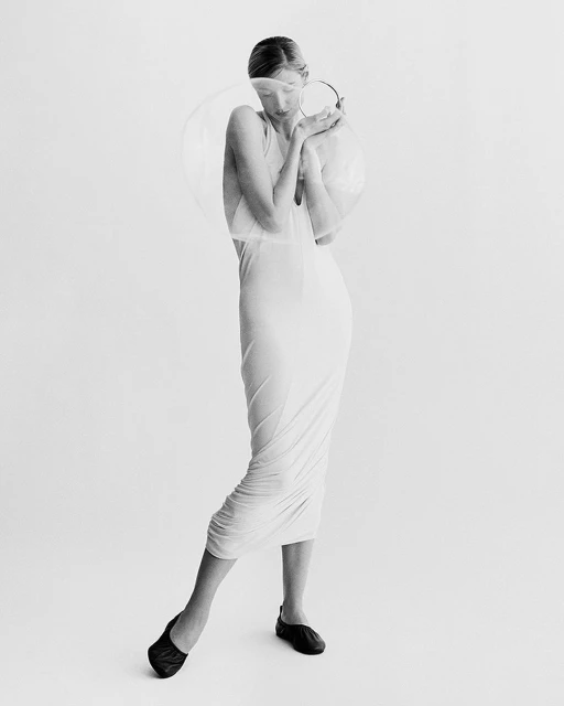 Elegant woman in a white dress poses in a photo studio with soft lighting and a minimalist aesthetic, creating a high-fashion editorial image.