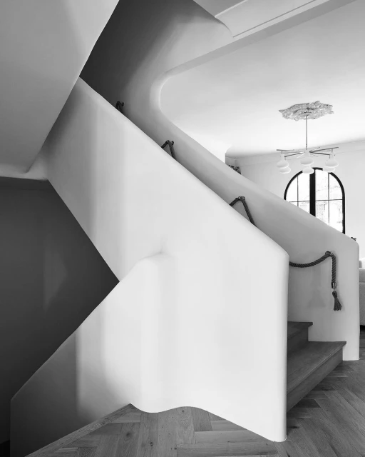 Monochrome photograph of a modern home interior showcasing a curved staircase, wooden floors, and a decorative ceiling light fixture.