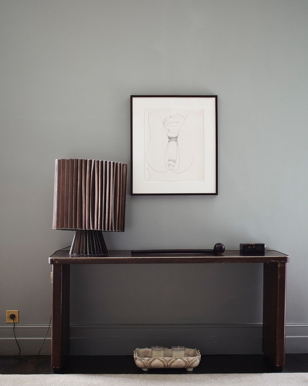 Interior view of a brown console table with a lamp, artwork, and accessories against a grey wall, creating a minimalist design.
