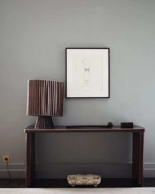 Interior view of a brown console table with a lamp, artwork, and accessories against a grey wall, creating a minimalist design.