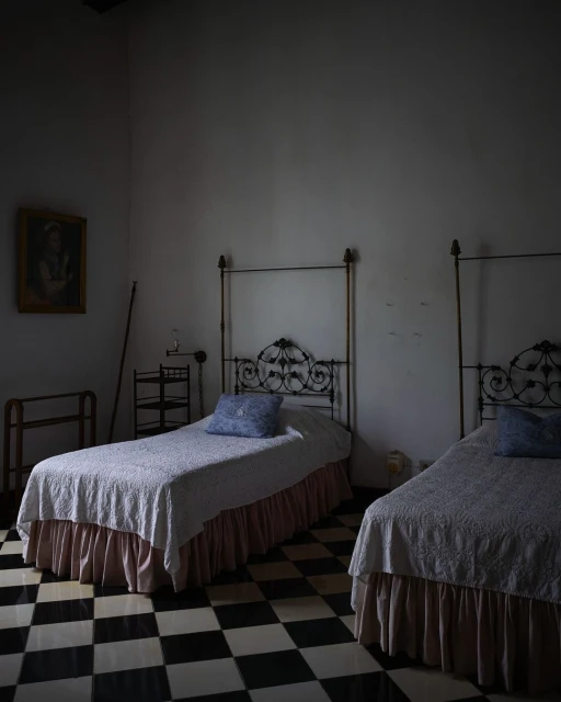Interior shot of a bedroom with two twin beds, black-and-white checkered floor, and vintage decor, creating a simple and quiet atmosphere.