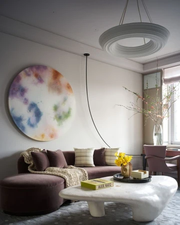Modern living room interior with a mauve velvet sofa, organic white stone coffee table, and large circular abstract wall art.