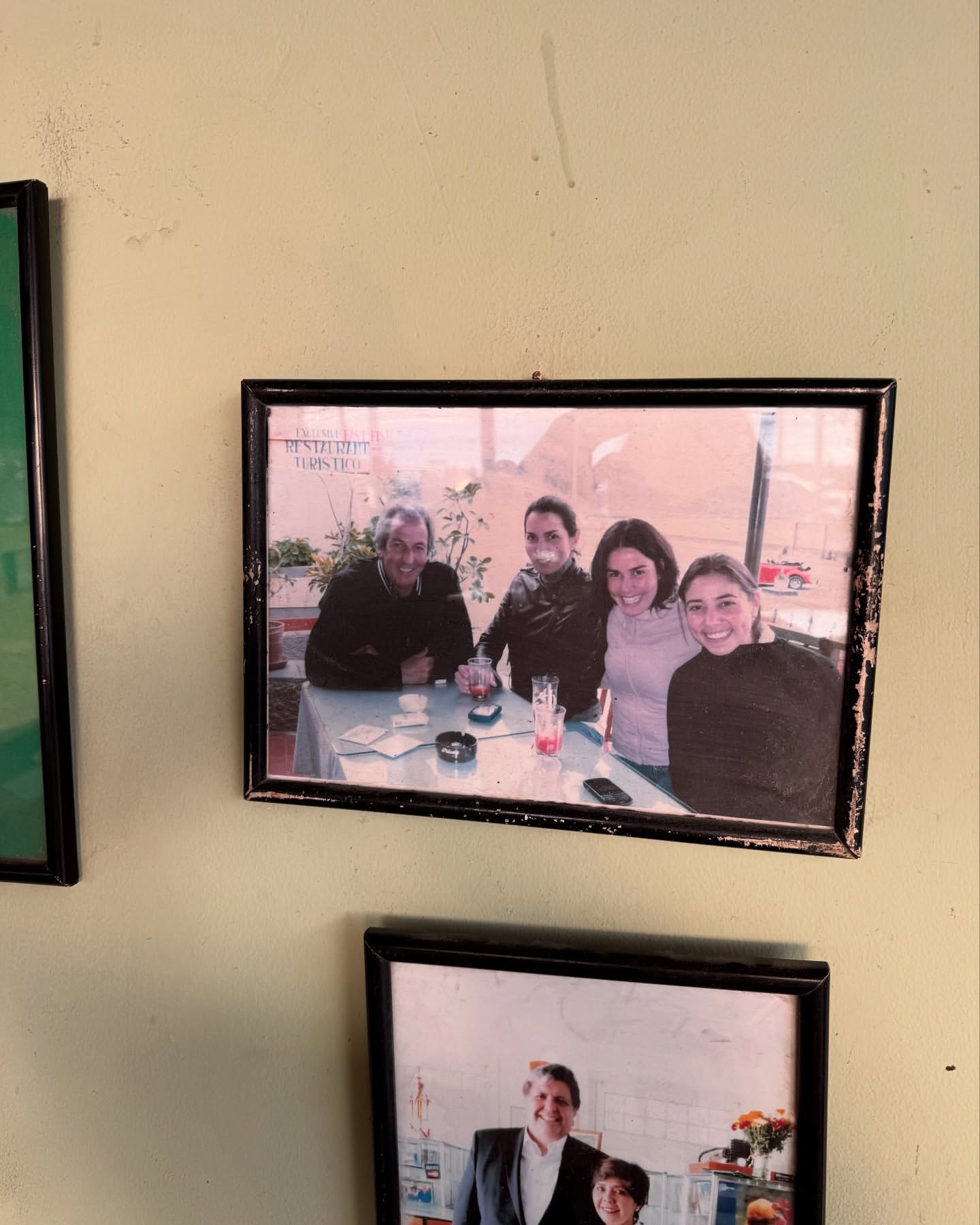 A framed photograph hanging on a wall showing four people sitting together around a table at an outdoor establishment.