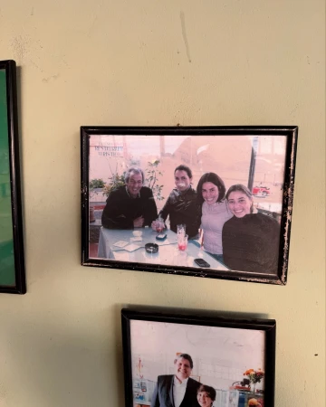 A framed photograph hanging on a wall showing four people sitting together around a table at an outdoor establishment.