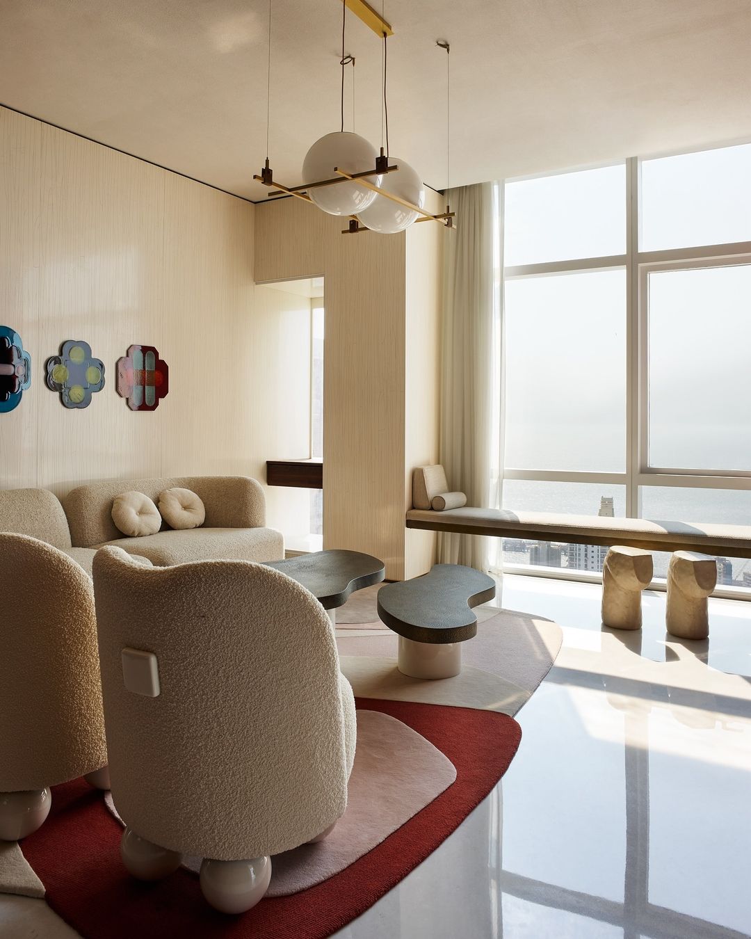 Contemporary living room featuring boucle armchairs, a curved sofa, unique coffee tables, modern pendant lighting, and a minimalist aesthetic.