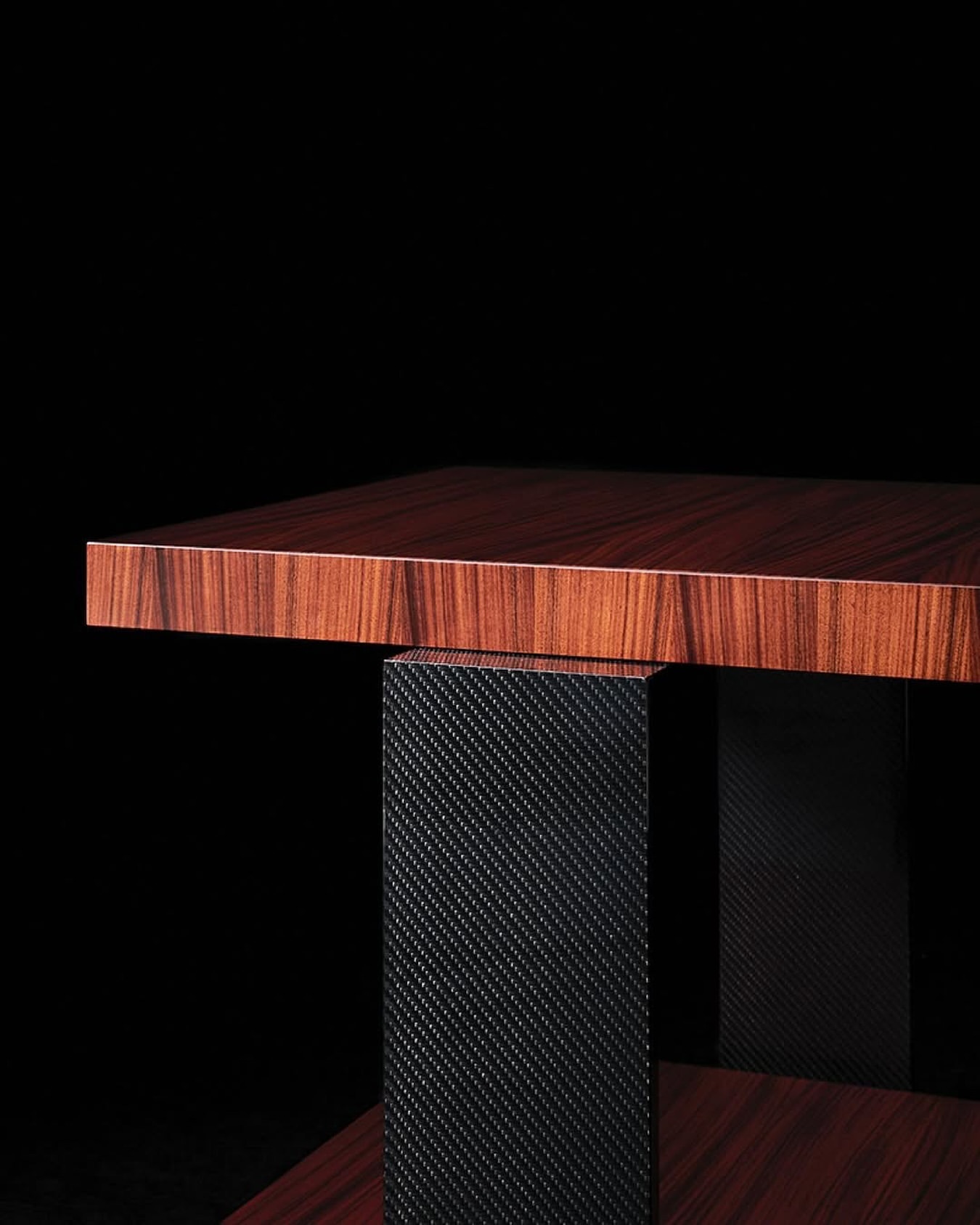 Close-up shot of a modern end table with a wood grain top and a dark, textured pedestal base against a stark black background.
