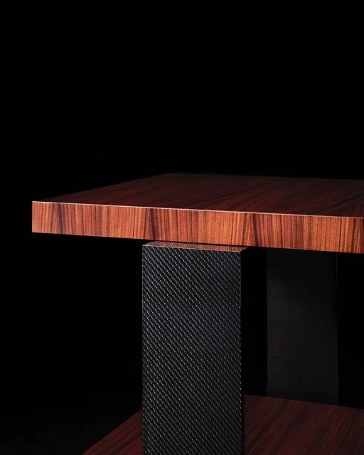 Close-up shot of a modern end table with a wood grain top and a dark, textured pedestal base against a stark black background.