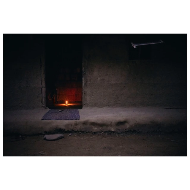 Dark, gritty interior shot with a lit candle providing the main light source. A doorway and rough wall textures are also visible.