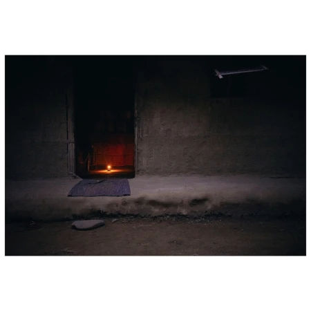 Dark, gritty interior shot with a lit candle providing the main light source. A doorway and rough wall textures are also visible.