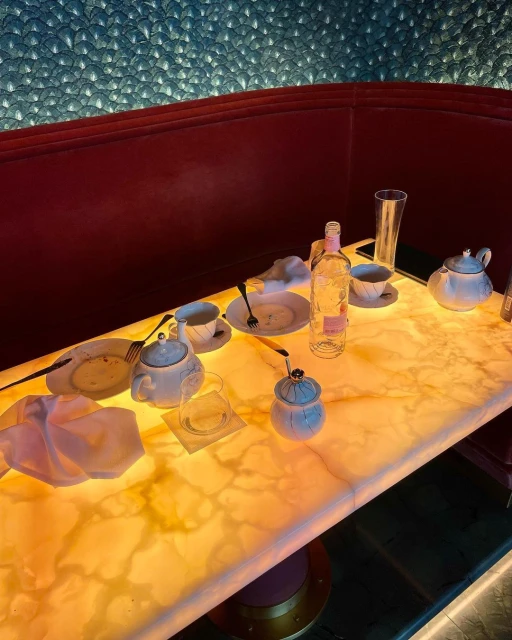 Illuminated table with used dishes, teacups, and a bottle, set against a decorative wall and booth seating in warm indoor light.