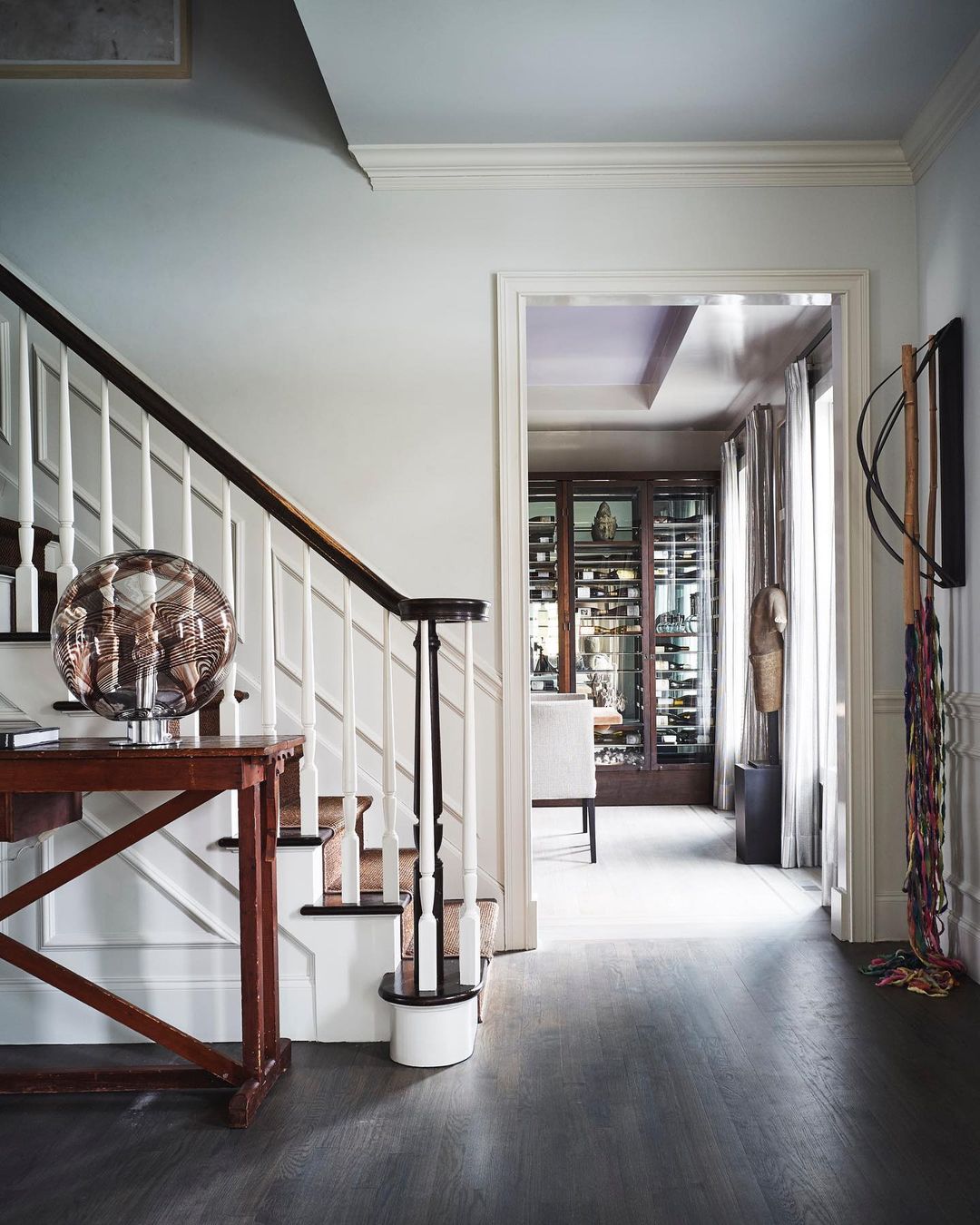 Indoor shot features a foyer with dark wood floors, white walls, staircase with white banister and dark wood railing, and an ornamental table lamp.