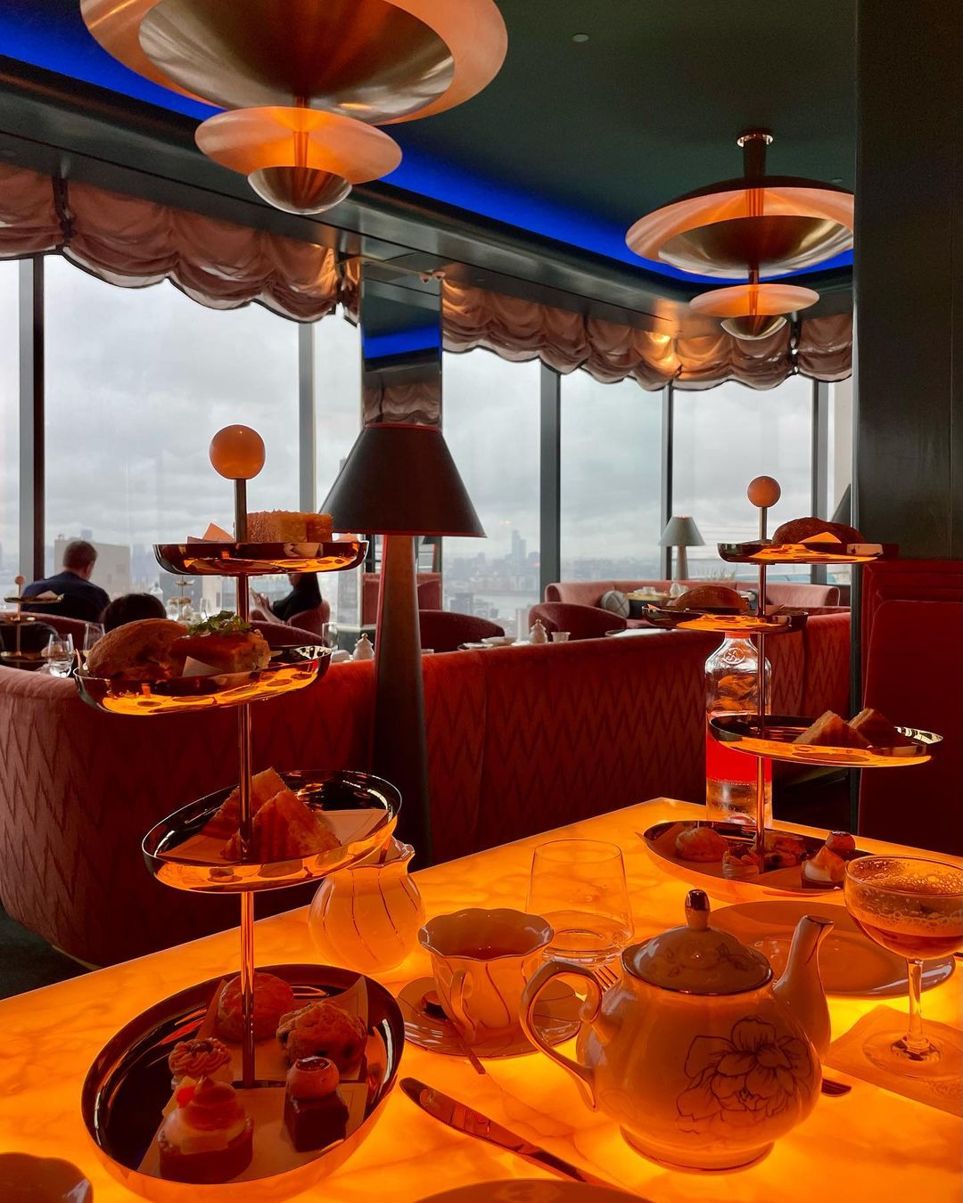 High-angle view of afternoon tea service, featuring tiers of pastries and snacks on a table with a teapot and drinks in a restaurant.