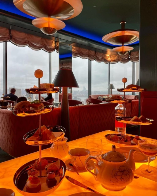 High-angle view of afternoon tea service, featuring tiers of pastries and snacks on a table with a teapot and drinks in a restaurant.