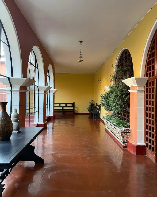 Indoor corridor with brown tile floor, yellow walls, arched doorways, hanging light, and antique table, creating a classic interior.
