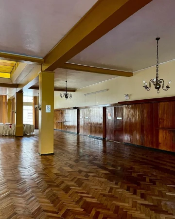 Spacious indoor venue featuring herringbone wood floors, paneled walls, decorative lighting, and high ceilings with supporting columns.