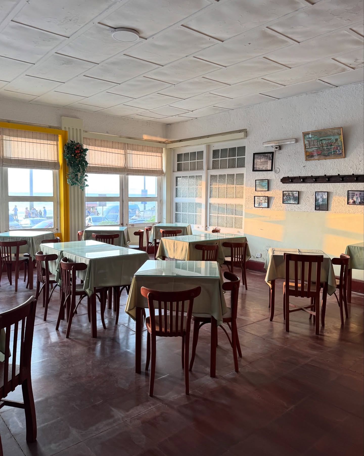 Interior of a restaurant with chairs and tables covered in cloths, illuminated by light coming through the windows.