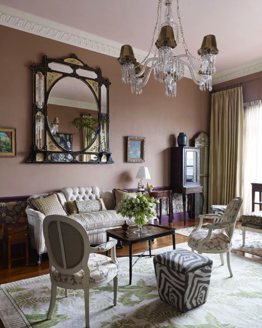 Living room with an antique mirror, tufted sofa, patterned chairs, area rug with leaf design, and a crystal chandelier.