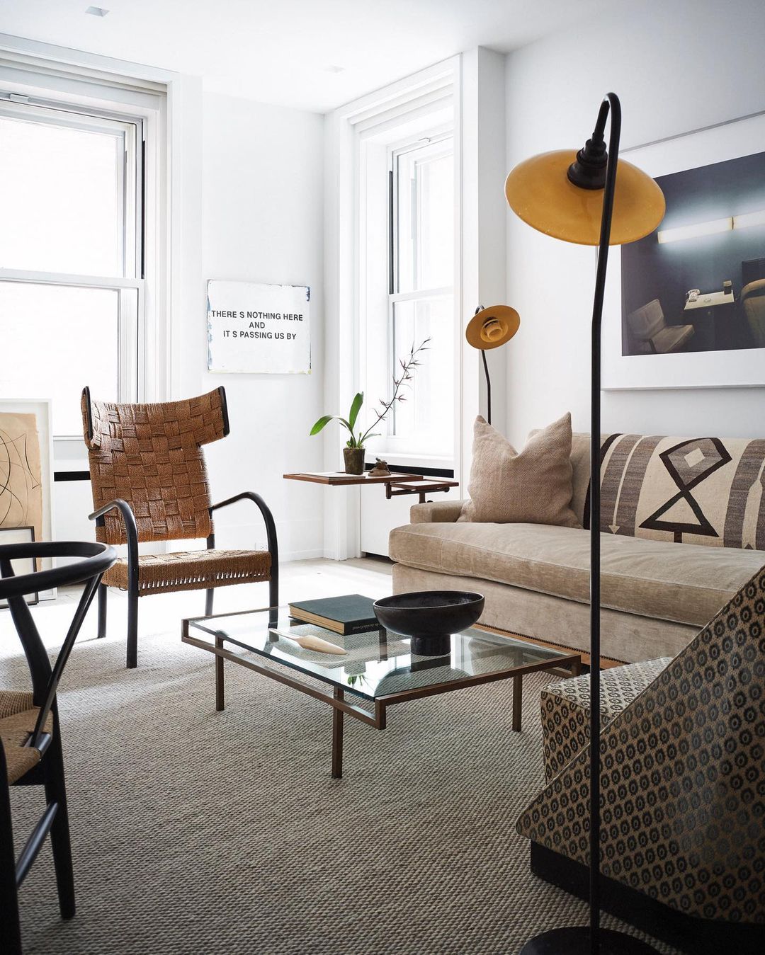 Living room interior featuring a brown woven chair, beige sofa with patterned pillows, coffee table, and modern lighting fixtures.