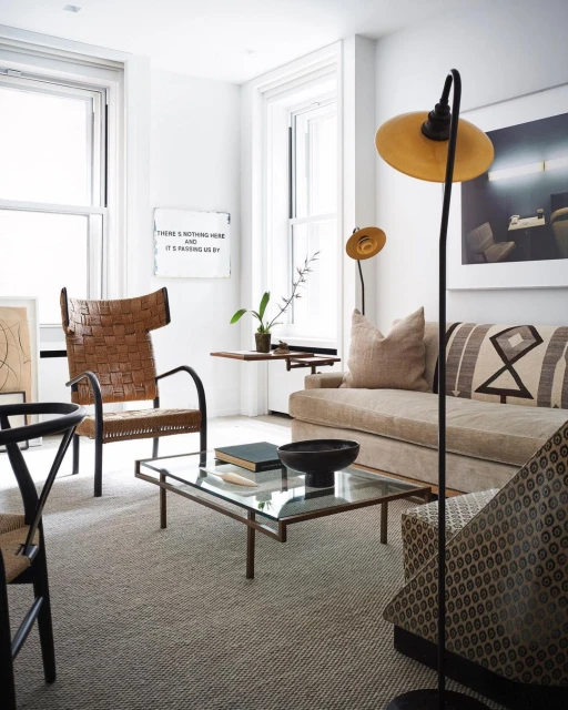Living room interior featuring a brown woven chair, beige sofa with patterned pillows, coffee table, and modern lighting fixtures.