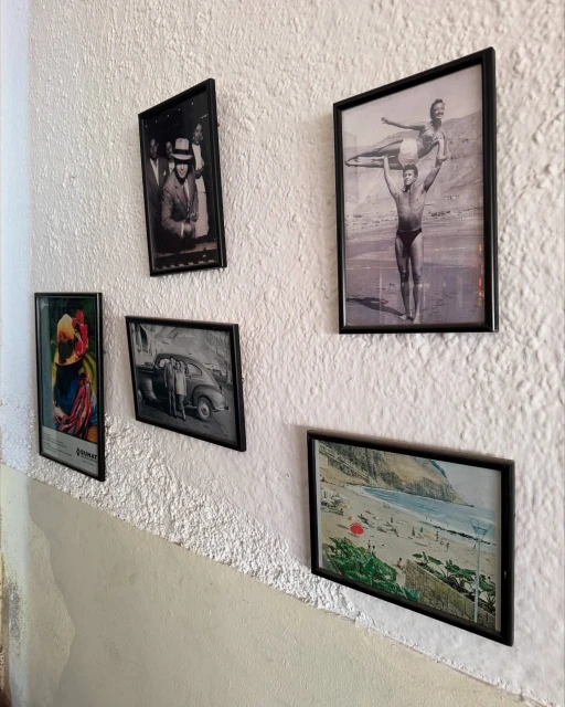 A textured white wall displays five framed photographs and art, including people, vintage cars, and a coastal beach scene in a room.