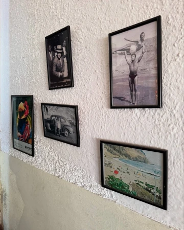 A textured white wall displays five framed photographs and art, including people, vintage cars, and a coastal beach scene in a room.