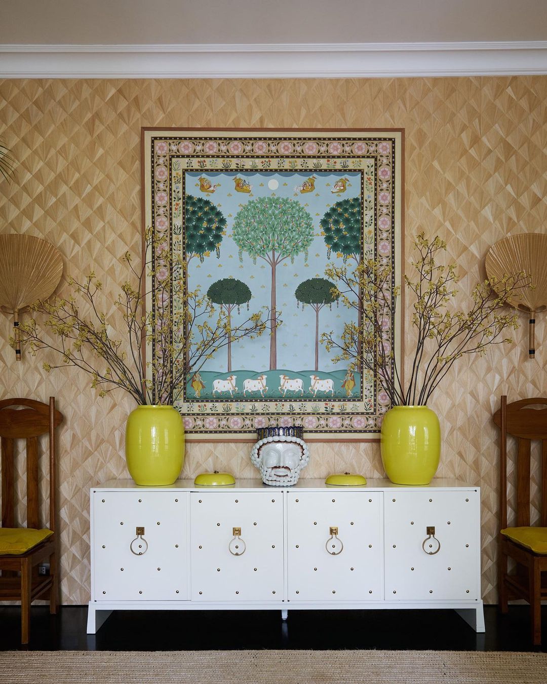 Interior view features a white sideboard beneath a framed painting, flanked by yellow vases and chairs in a room with textured wallpaper.