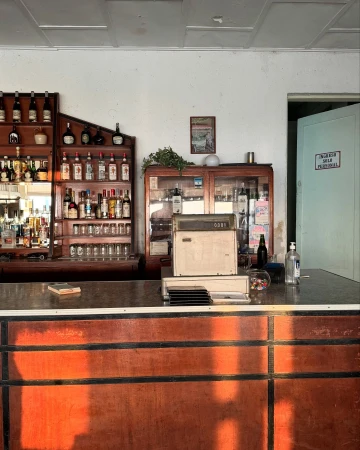 Interior view of a vintage bar with shelves of bottles, a cash register, and a wooden counter in warm light, creating an inviting atmosphere.