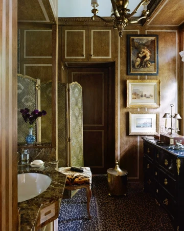 Ornate bathroom interior featuring a marble sink, animal print stool, decorative screen, and antique gold accents.