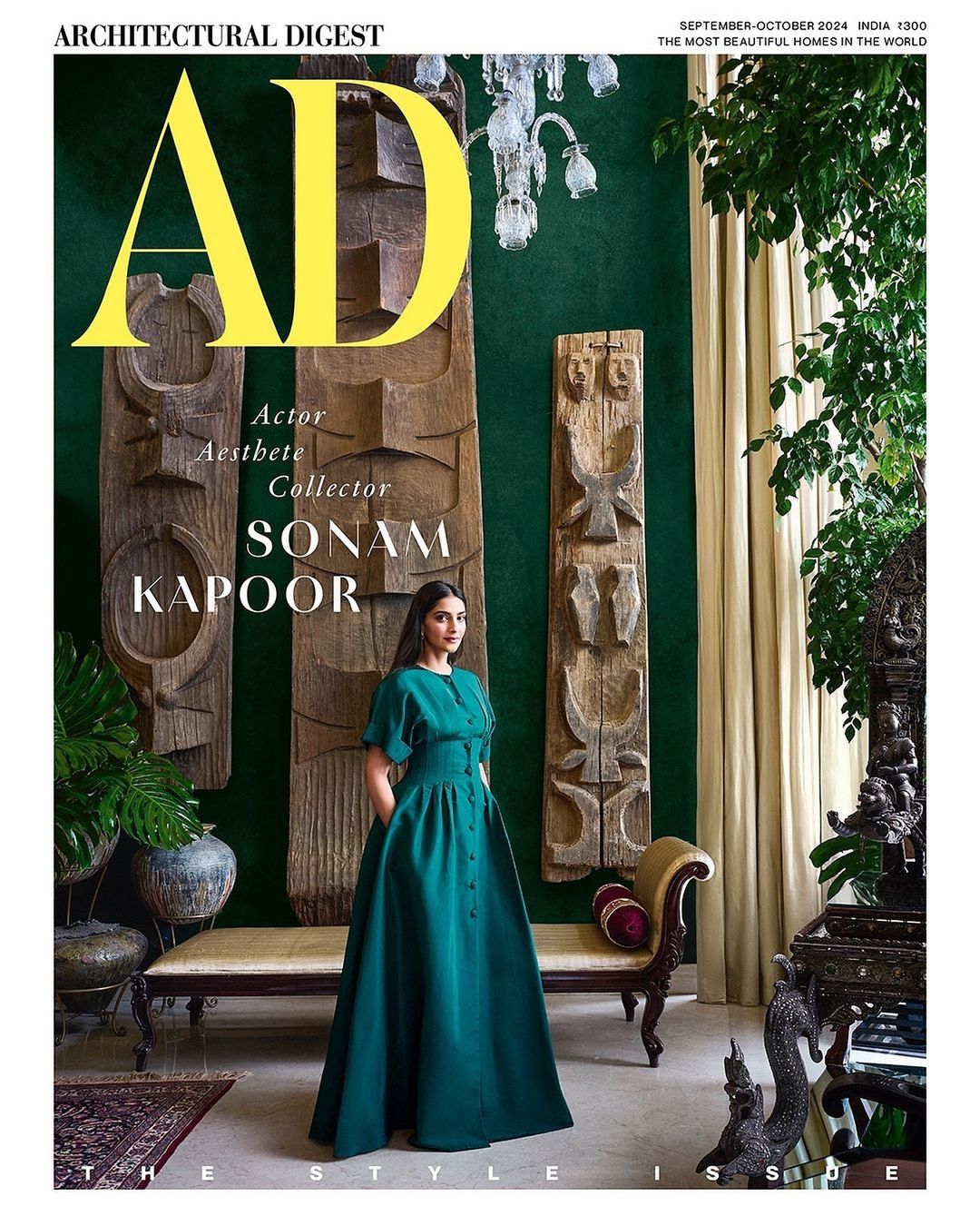 Sonam Kapoor in emerald dress on Architectural Digest cover. Indoor studio with decorative objects, table, and sculptures create backdrop.