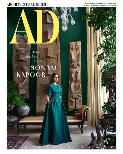 Sonam Kapoor in emerald dress on Architectural Digest cover. Indoor studio with decorative objects, table, and sculptures create backdrop.