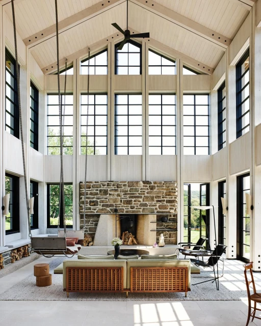 Living room interior with stone fireplace, wooden accents, and large windows, creating a bright and airy atmosphere in the home space.