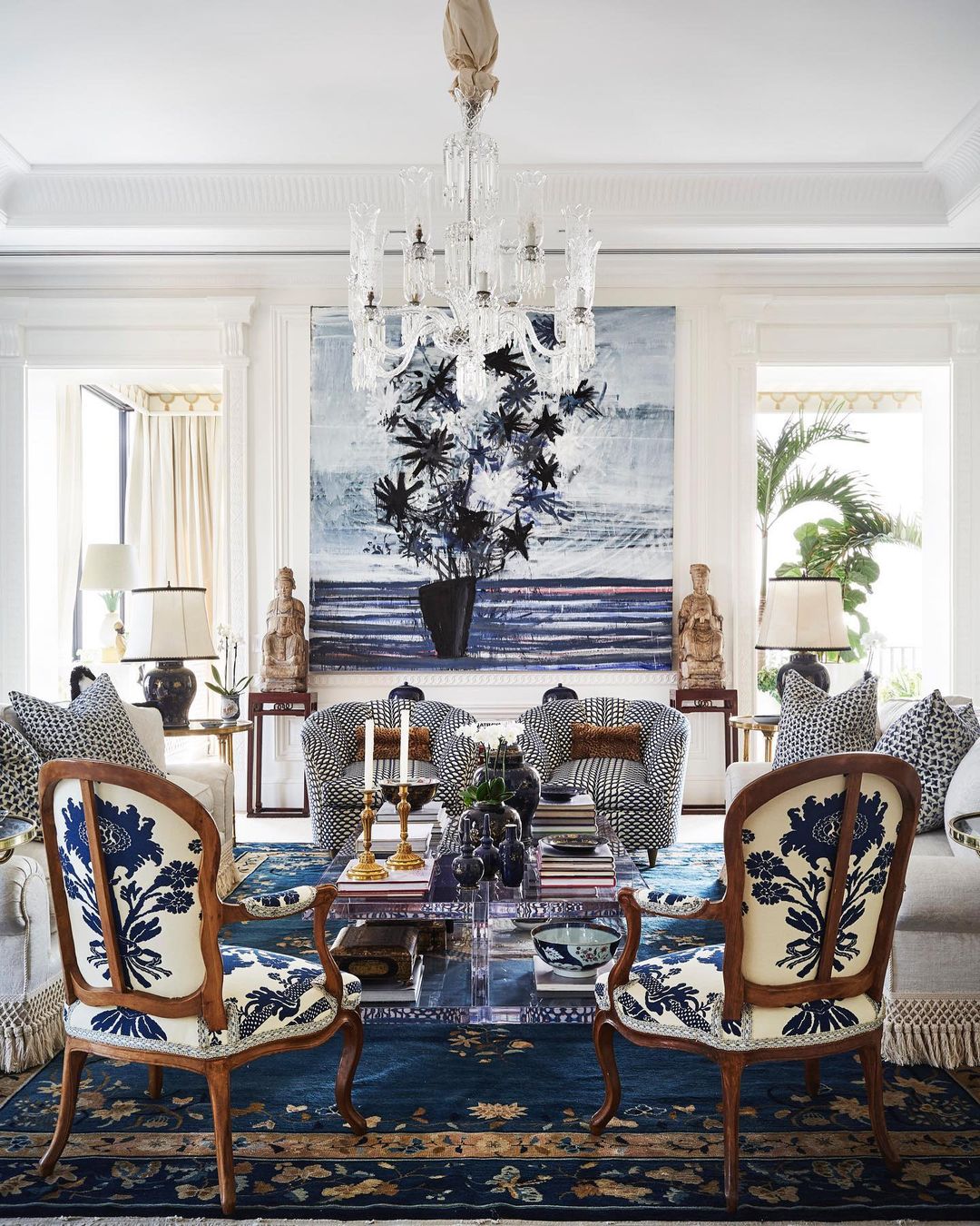 Elegant living room interior with blue and white patterned chairs and sofa, decorative artwork, crystal chandelier, and interior design details.