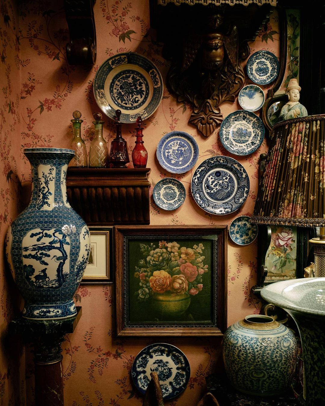Intricate display of blue and white porcelain plates and vases adorns a peach-colored wall with floral wallpaper and framed artwork.