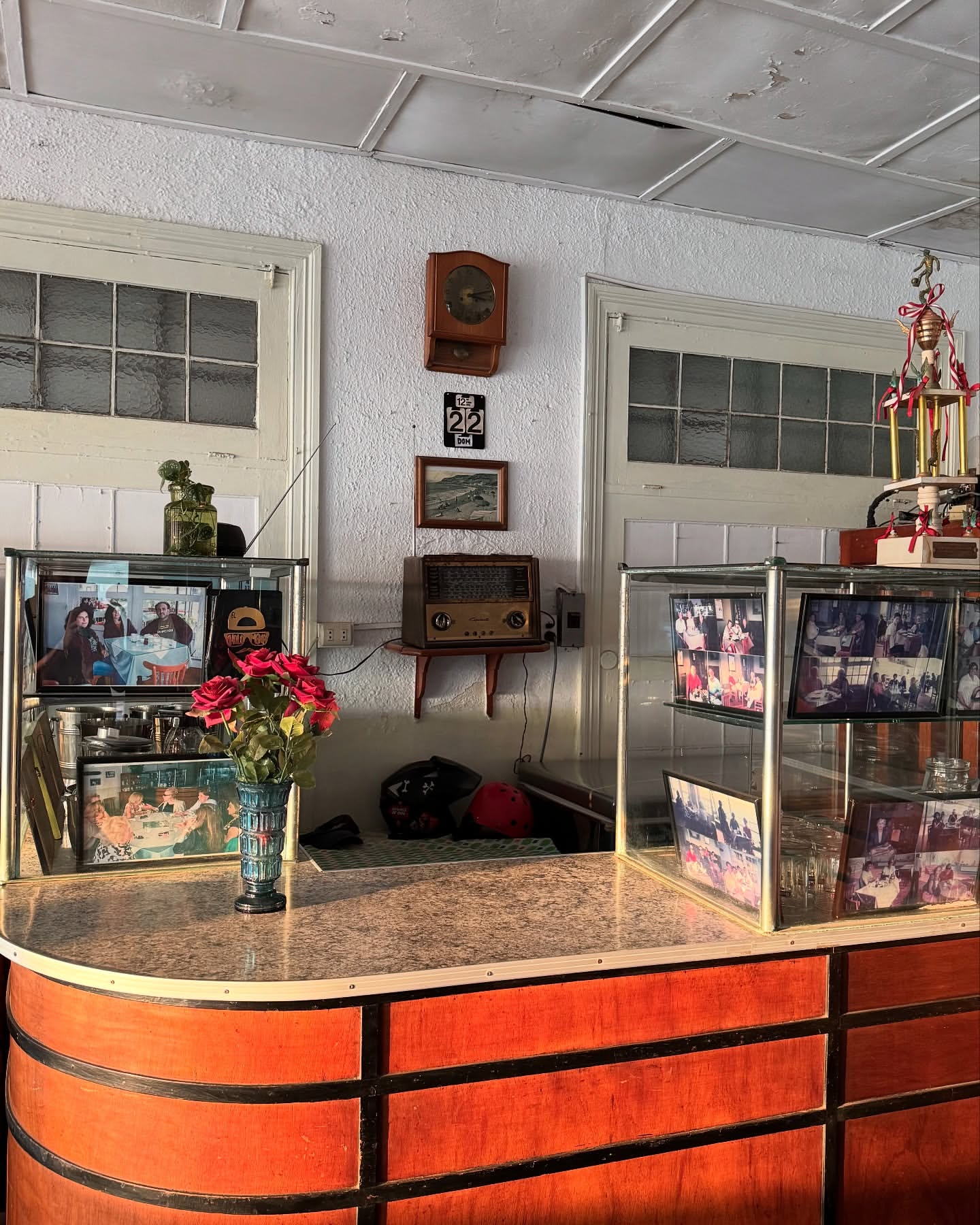 Interior view of a diner counter with vintage decorations, including floral arrangements, framed photos, and retro radio equipment.