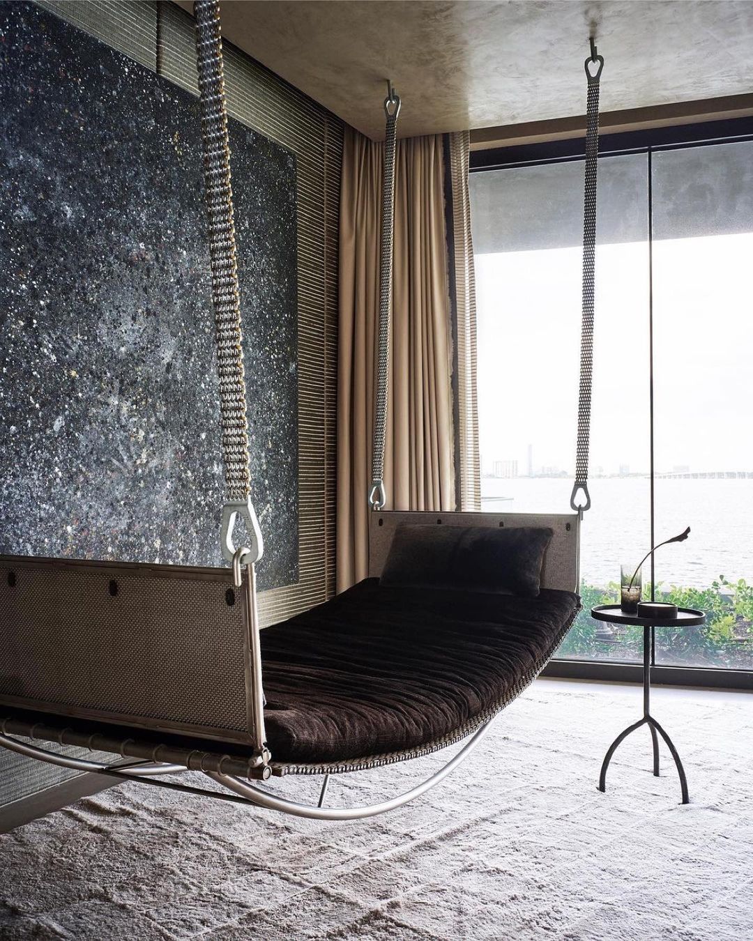 Bedroom interior with a suspended bed, side table, and a large window overlooking the water, creating a modern and serene sleeping space.