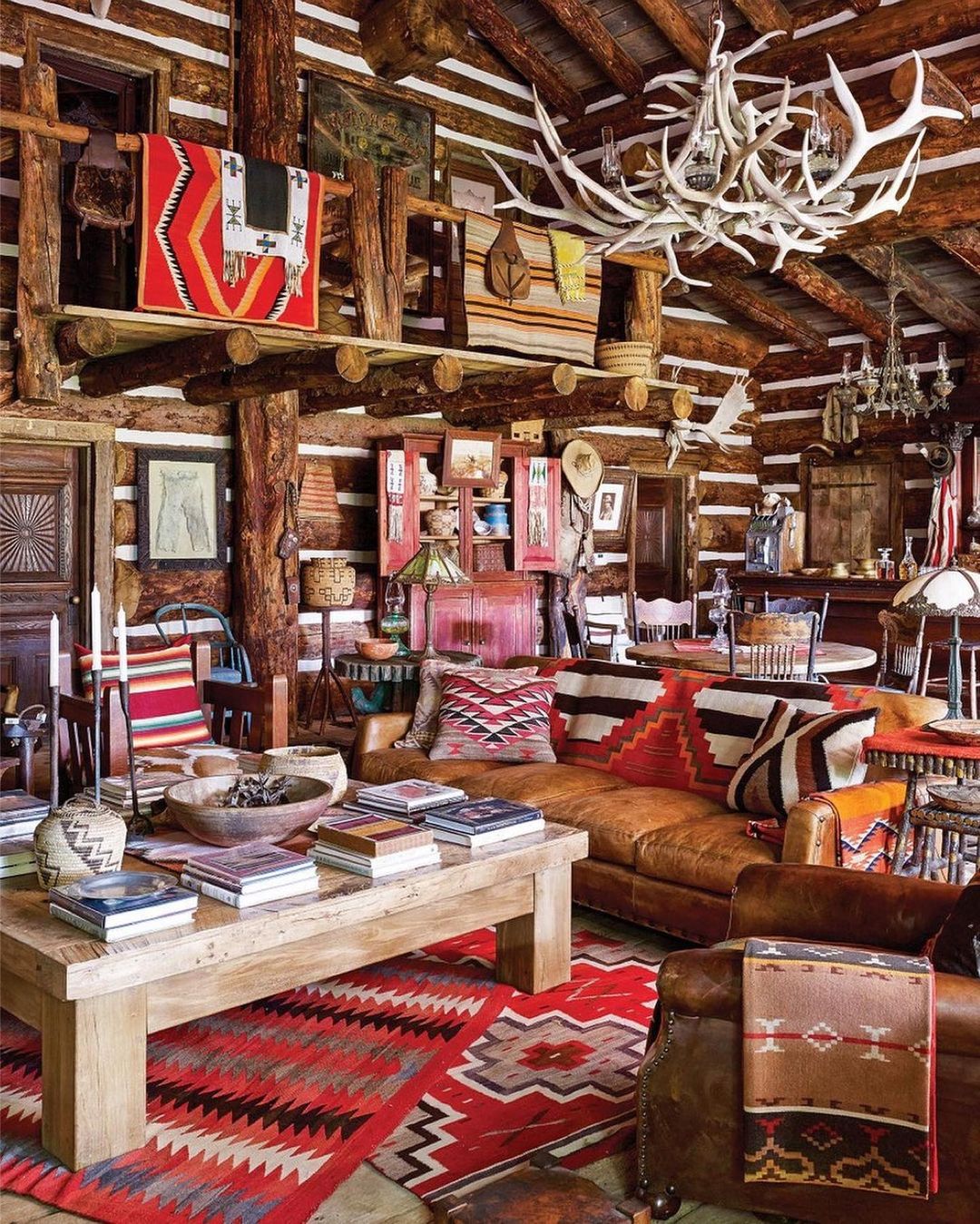 Rustic living room interior featuring a wooden coffee table with books, a leather sofa, and a decorative antler chandelier.