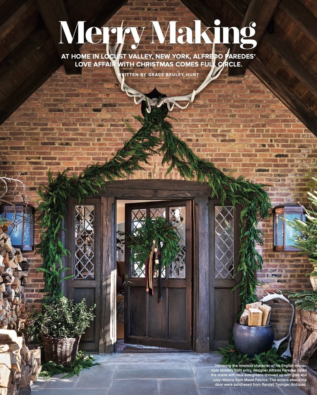 Exterior of a brick home with an open wooden door decorated with a wreath and garland. Antlers hang above the door.