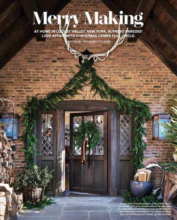 Exterior of a brick home with an open wooden door decorated with a wreath and garland. Antlers hang above the door.
