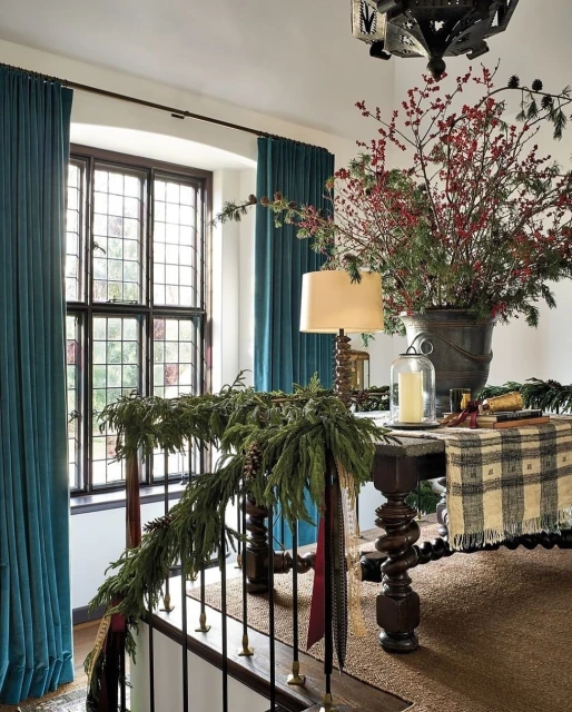 Festive foyer interior with a dark wood table displaying red berries, green garland, and a plaid throw with a traditional aesthetic.