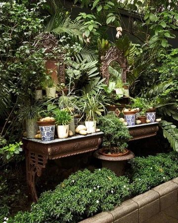 Indoor garden display featuring ornate metal tables holding potted plants and stone pebbles surrounded by lush green foliage.