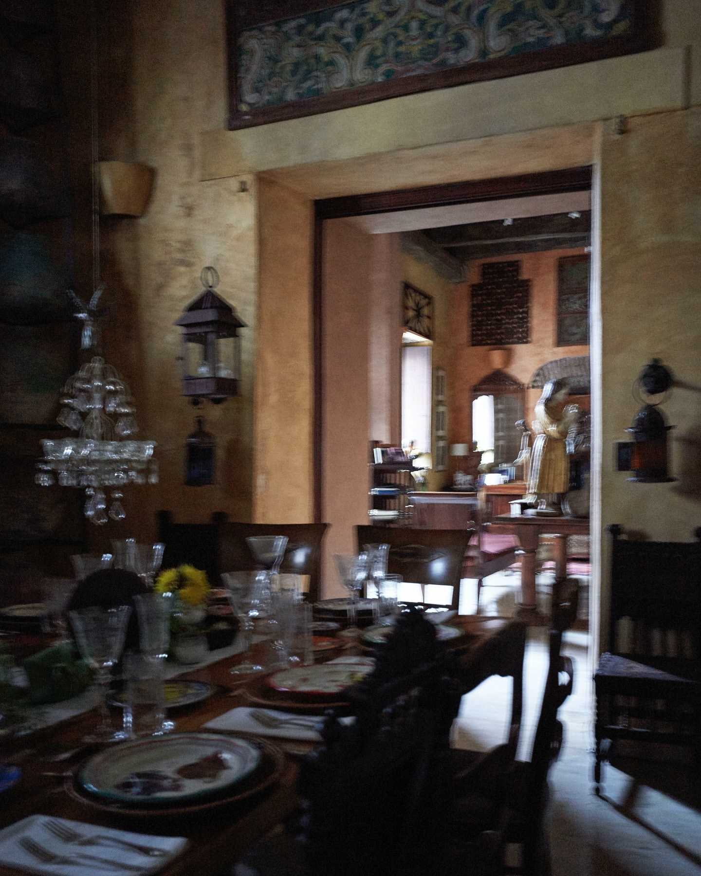 Ornate dining room interior with a long table set for a meal, featuring tableware, chairs, chandelier, and decorative elements in warm lighting.