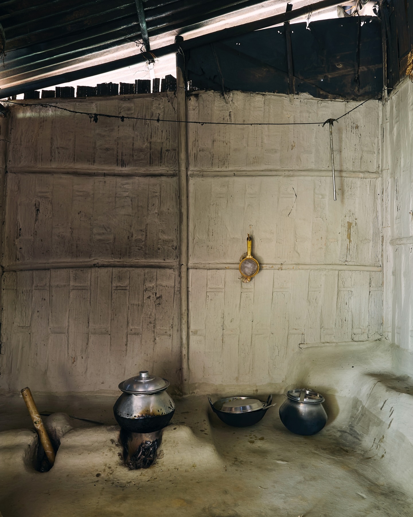Rustic kitchen scene with traditional metal cookware on a stove, set against a textured wall in an indoor, simple cooking environment.