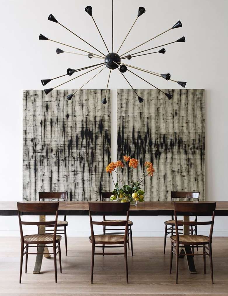 Modern dining room with wooden table and chairs, minimalist art, and a statement starburst chandelier creating an elegant interior.